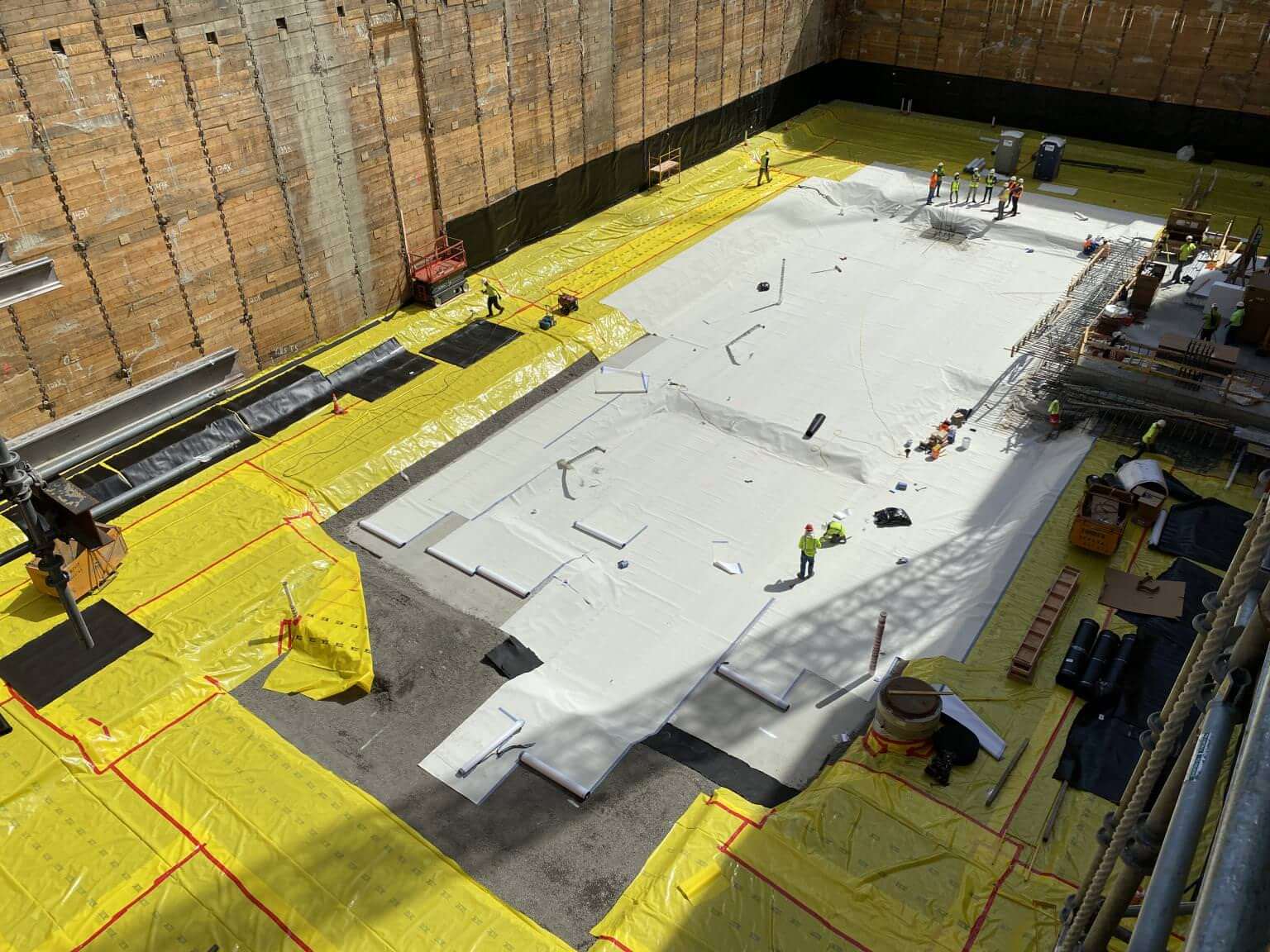 Workers installing sheet waterproofing membrane over concrete slab foundation